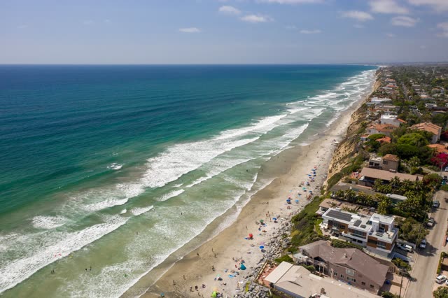 Aerial view of the beach, the surf and palm trees at Moonlight Beach, with a crowd gathered.