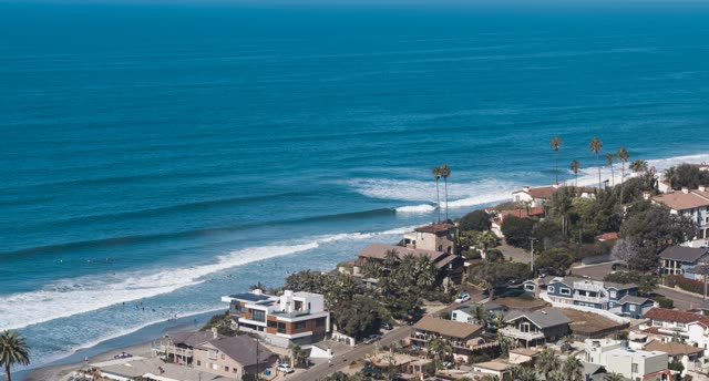 Aerial view of the beach, the surf and palm trees at Moonlight Beach, with surfers out.