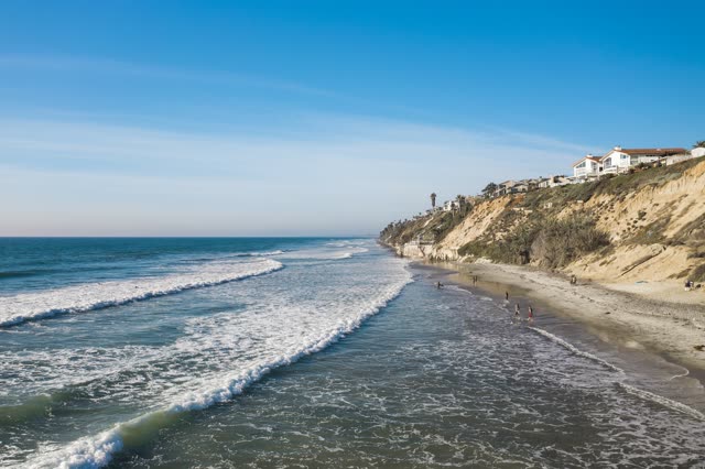 Low aerial view of the beach, the surf and the ocean in Encinitas, with people walking.