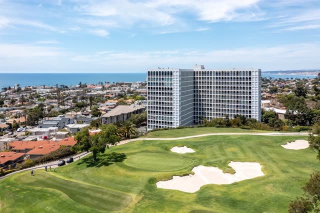 Aerial view of a residential street, palm trees and the ocean at La Jolla Country Club, with people walking.
