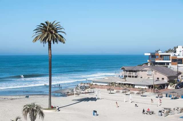 Elevated view of the beach, the surf and palm trees at Moonlight Beach, with people walking.