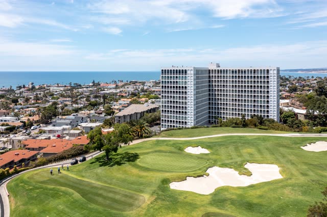 Aerial view of a residential street, palm trees and the ocean at La Jolla Country Club, with people walking.