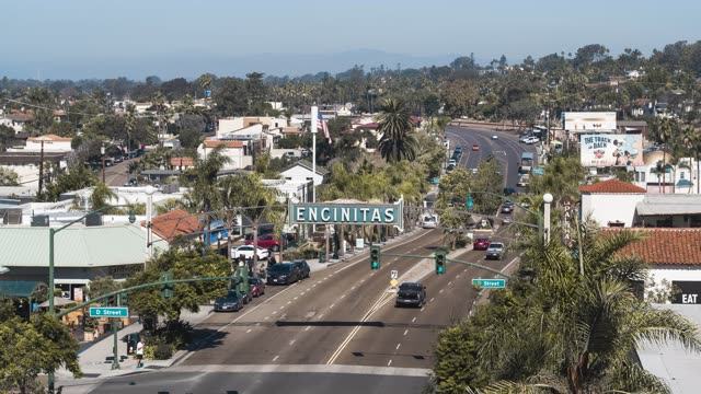 Low aerial view of the downtown streets, palm trees and homes at Downtown Encinitas, with people walking.