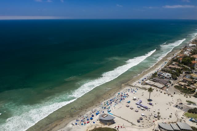 Aerial view of the beach, the surf and the ocean at Moonlight Beach, with a crowd gathered.