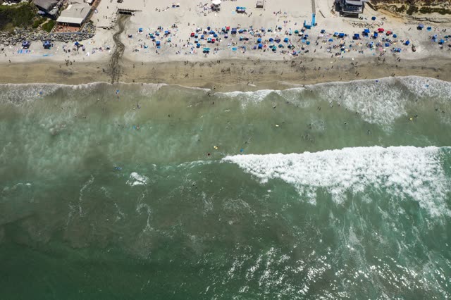 Aerial view of the beach, the surf and the ocean at Moonlight Beach, with swimmers in the water.