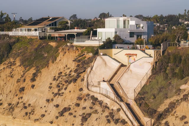 Low aerial view of the cliffs, palm trees and homes in Encinitas, with people walking.