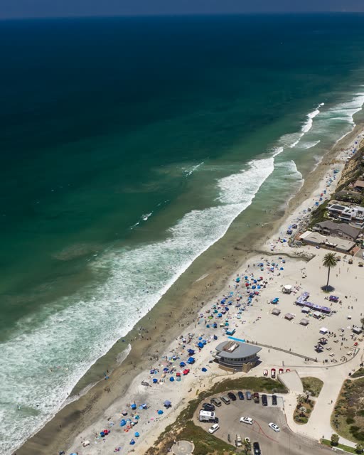 Aerial view of the beach, the surf and the ocean at Moonlight Beach, with a crowd gathered.