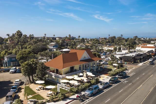 Low aerial view of a residential street, palm trees and homes in Encinitas, with people eating outside.