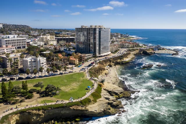 Aerial view of the cliffs, palm trees and the ocean at La Jolla Cove, with people walking.