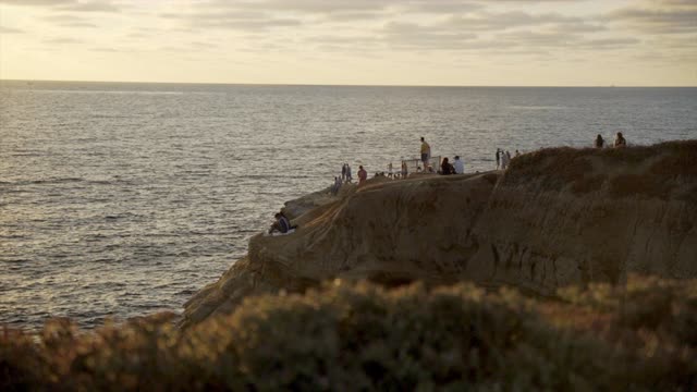 Elevated view of the cliffs, the ocean and open country at Sunset Cliffs, with a crowd gathered.