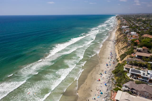 Aerial view of the beach, the surf and the ocean at Moonlight Beach, with swimmers in the water.