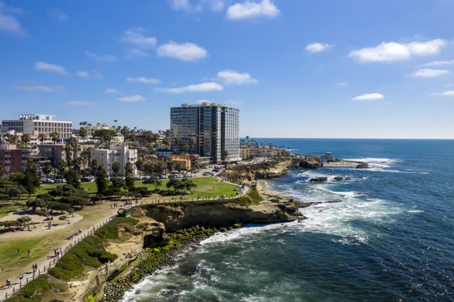 Aerial view of the cliffs, palm trees and the ocean at La Jolla Cove, with people walking.
