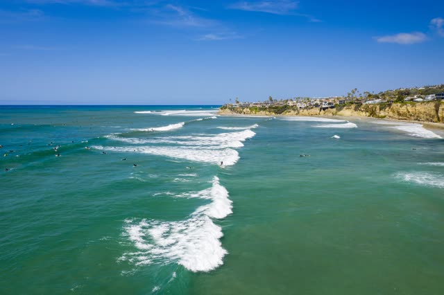 Low aerial view of the beach, the surf and the ocean in Pacific Beach, with surfers out.