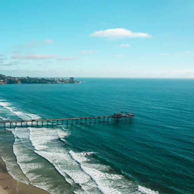 Aerial view of the beach, the surf and the pier at La Jolla Farms, with people walking.