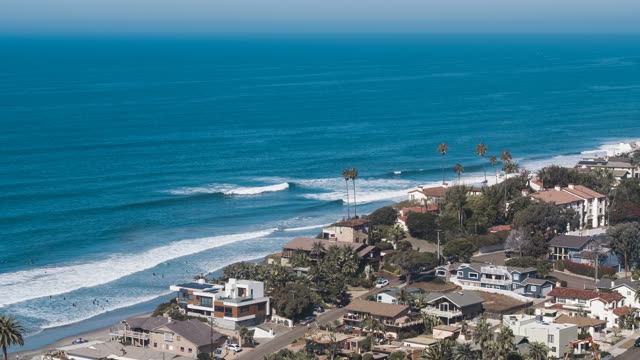 Aerial view of the beach, the surf and palm trees at Moonlight Beach, with surfers out.