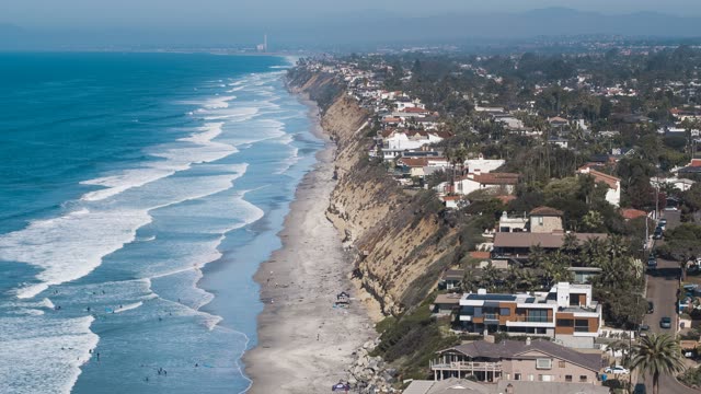 Aerial view of the cliffs, the surf and palm trees at Moonlight Beach, with surfers out.