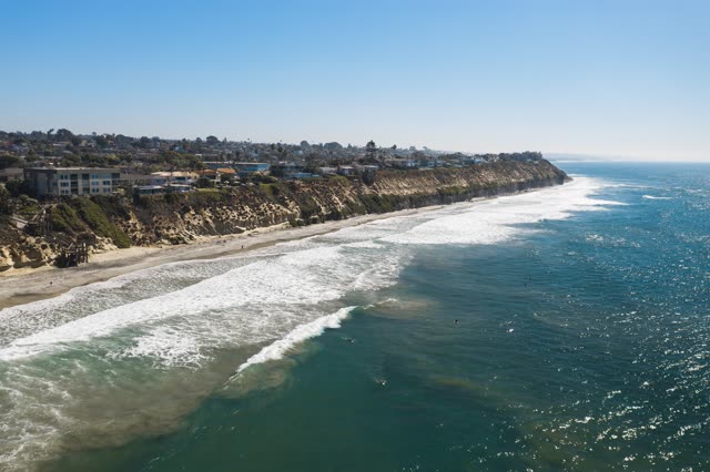Aerial view of the cliffs, the surf and the ocean in Encinitas, with surfers out.