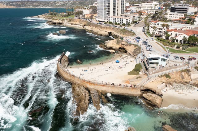 Aerial view of the cliffs, the surf and the ocean at La Jolla Cove, with a crowd gathered.
