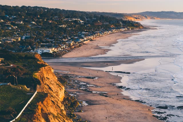 Aerial view of the cliffs, the surf and the ocean in Del Mar, with people walking.