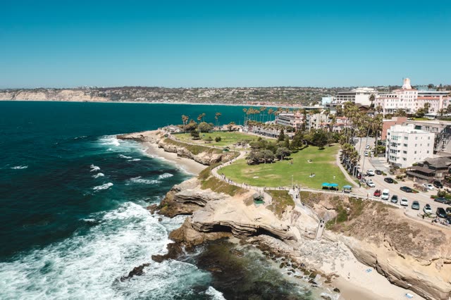 Aerial view of the cliffs, the surf and palm trees at La Jolla Cove, with people walking.