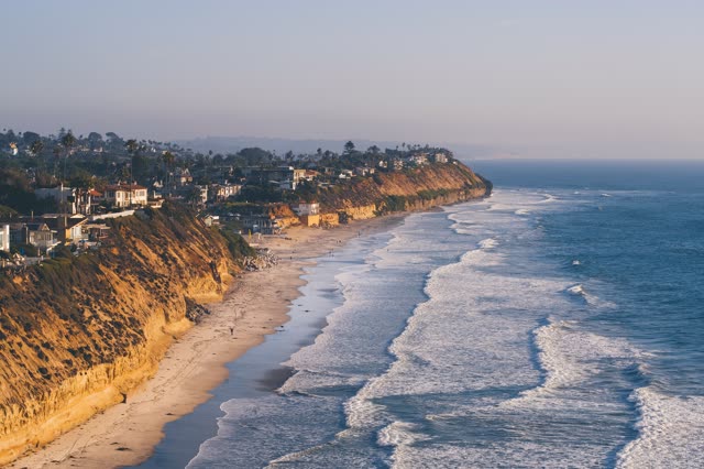 Aerial view of the cliffs, the surf and palm trees in Encinitas, with people walking.