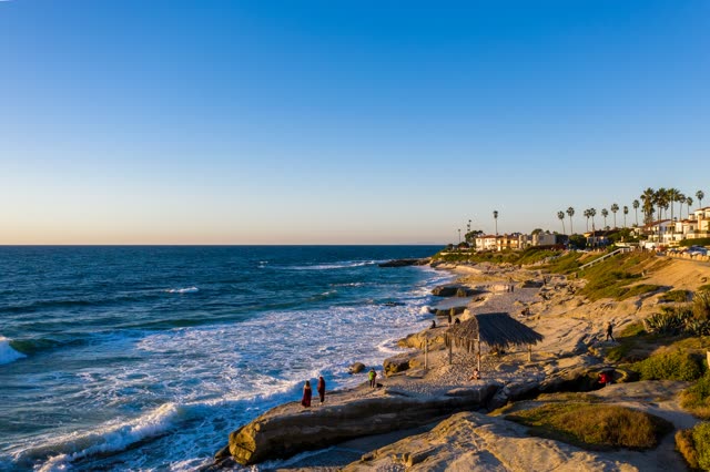 Elevated view of the cliffs, the surf and palm trees at Windansea, with people walking.