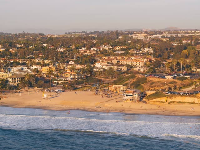 Aerial view of the beach, the surf and palm trees at Moonlight Beach, with people walking.
