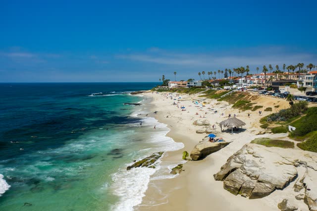 Aerial view of the beach, the surf and palm trees at Windansea, with people walking.