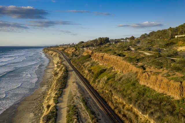 Aerial view of the cliffs, the surf and the ocean in Del Mar, with people walking.