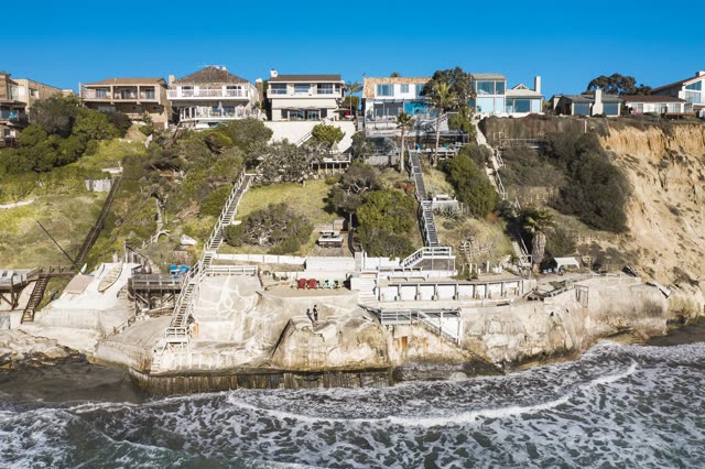 Low aerial view of the cliffs, the surf and palm trees in Encinitas, with people walking.