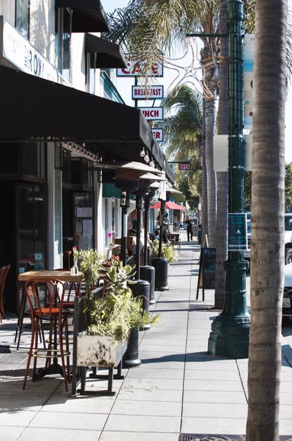 The downtown streets, palm trees and the buildings at Downtown Encinitas, with people eating outside.