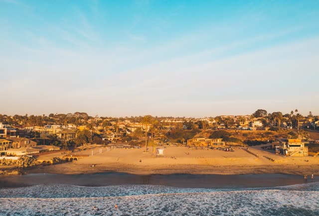 Low aerial view of the beach, the surf and palm trees at Moonlight Beach, with people walking.