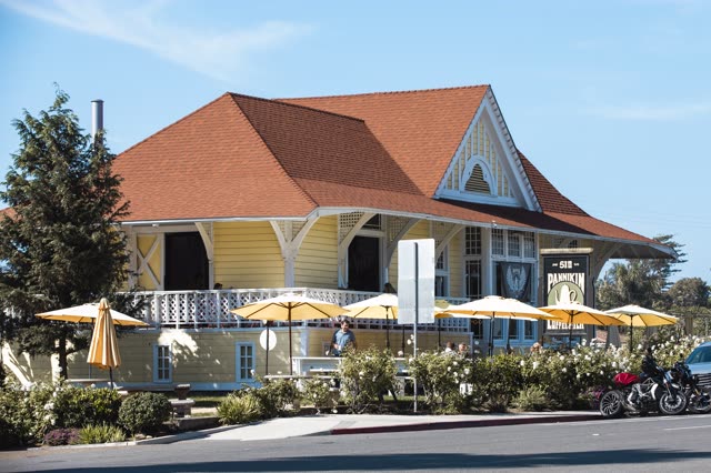 The downtown streets, the buildings and traffic in Encinitas, with people eating outside.