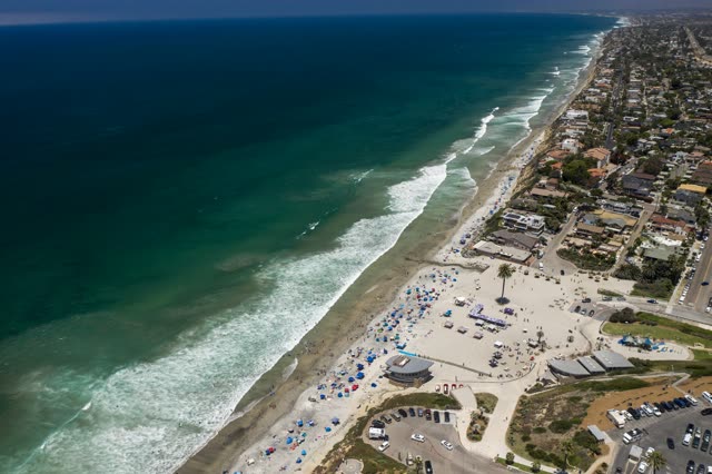 Aerial view of the beach, the surf and the ocean at Moonlight Beach, with a crowd gathered.