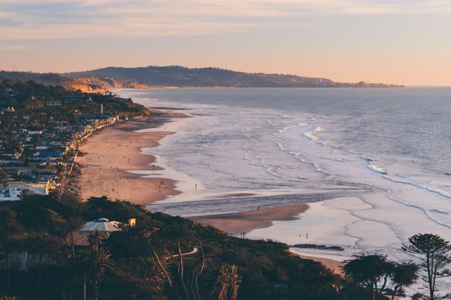 Elevated view of the cliffs, the surf and palm trees in Del Mar, with people walking.