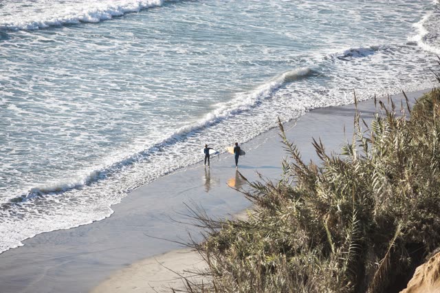 Low aerial view of the cliffs, the surf and the ocean in Encinitas, with people walking.