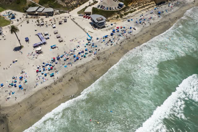 Aerial view of the beach, the surf and palm trees at Moonlight Beach, with a crowd gathered.
