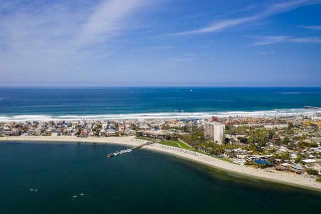 Aerial view of the beach, the surf and the pier in Mission Bay, with paddlers on the water.