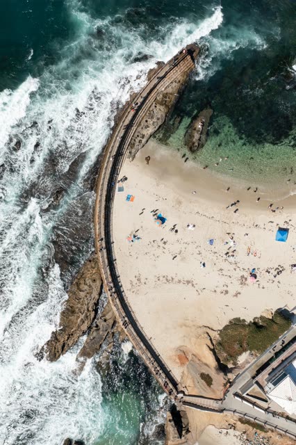 Aerial view of the beach, the surf and the ocean at La Jolla Cove, with a crowd gathered.