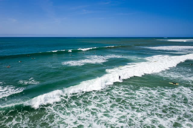Low aerial view of the beach, the surf and the ocean in Pacific Beach, with surfers out.