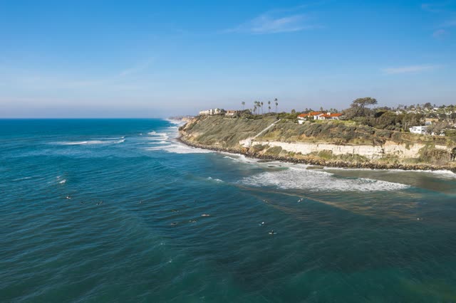 Aerial view of the cliffs, the surf and palm trees at Swamis, with surfers out.