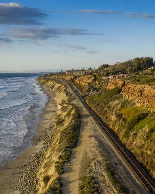 Aerial view of the cliffs, the surf and the ocean in Del Mar, with people walking.