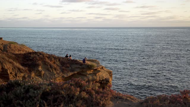Elevated view of the cliffs, the ocean and open country at Sunset Cliffs, with a crowd gathered.