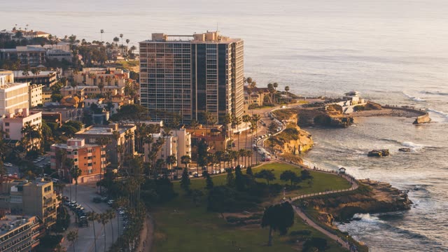 Aerial view of the cliffs, palm trees and the ocean at La Jolla Cove, with people walking.