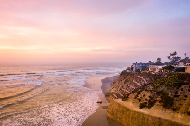 Aerial view of the cliffs, the surf and palm trees in Solana Beach, with people walking.