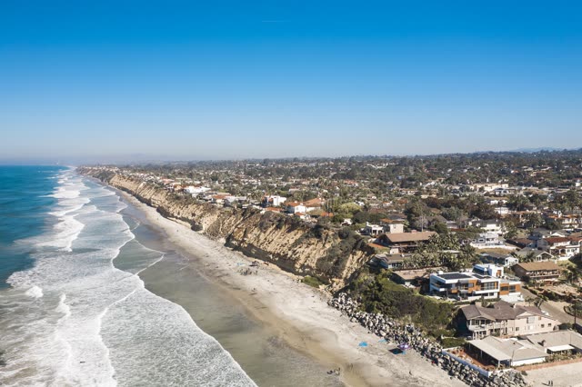 Aerial view of the cliffs, the surf and the ocean at Moonlight Beach, with people walking.