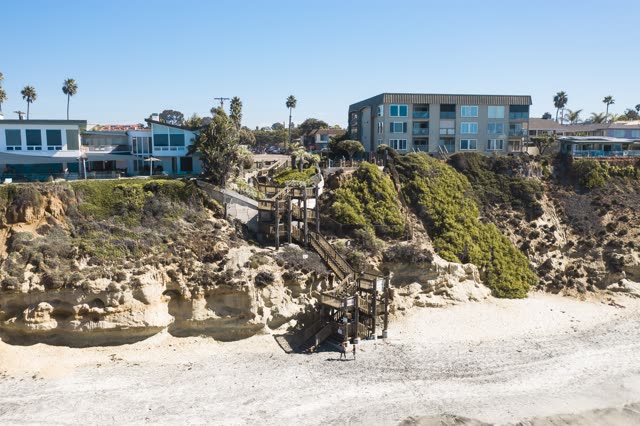 Low aerial view of the cliffs, palm trees and homes in Encinitas, with people walking.