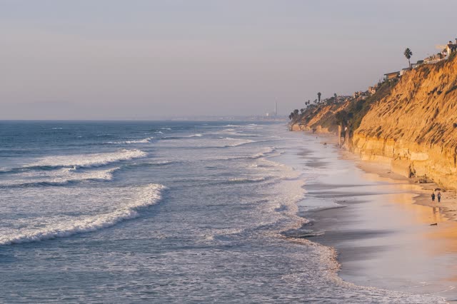 The beach, the surf and palm trees in Encinitas, with people walking.