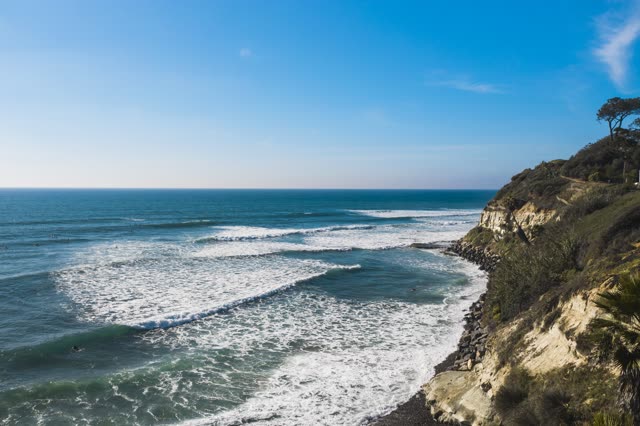 Elevated view of the cliffs, the surf and palm trees at Swamis, with surfers out.