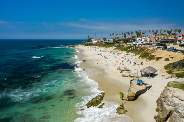 Aerial view of the beach, the surf and palm trees at Windansea, with people walking.